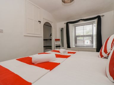 A bedroom with a bed with red and white striped linens two rolled towels on the bed a window with blinds and black curtains at Walter in Newlyn