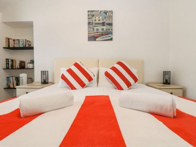 A bedroom with a bed with red and white striped bedding and pillows with shelves of books on the side at Walter in Newlyn