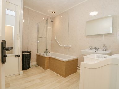 A bathroom with a bathtub shower combination a sink a mirror and a black laundry basket at Walter in Newlyn