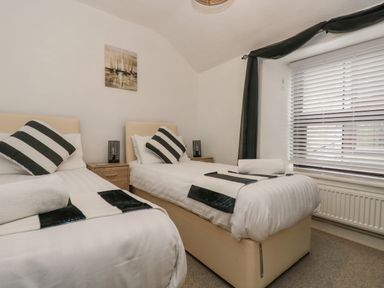 A bedroom with two single beds each with striped pillows a window with blinds and curtains and a painting on the wall at Walter in Newlyn