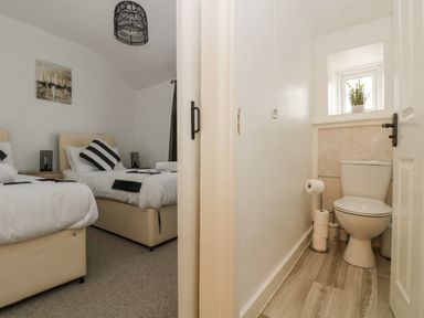 A bedroom with two single beds and a bathroom with a toilet and a small window at Walter in Newlyn