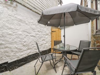 An outdoor patio area with a round glass table four chairs a large umbrella and a wooden gate at Walter in Newlyn