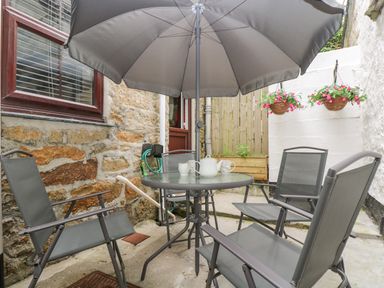 Outdoor patio area with round glass table and four chairs under a grey umbrella at Walter in Newlyn