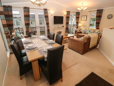 A dining area with a table set for six and a living room with two brown sofas and a wall-mounted tv at 16 Heritage Park Heritage Park near Kilgetty