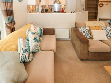 A living room with two sofas with patterned pillows and a view into a kitchen at 16 Heritage Park Heritage Park near Kilgetty