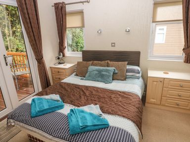 A bedroom with a bed, bedside tables, windows with curtains, and a glass door leading outside at 16 Heritage Park Heritage Park near Kilgetty