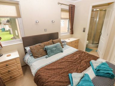 A bedroom with a double bed, bedside tables, windows, and an attached bathroom at 16 Heritage Park Heritage Park near Kilgetty