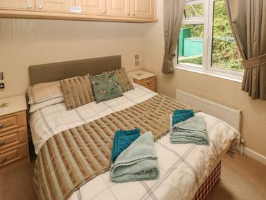 A bedroom with a double bed pillows folded towels bedside cabinets and a window with curtains at 16 Heritage Park Heritage Park near Kilgetty