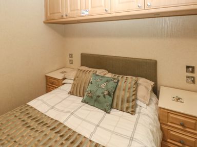 A bedroom with a bed with striped pillows and overhead wooden cabinets at 16 Heritage Park Heritage Park near Kilgetty