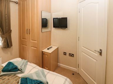 A bedroom corner with a bed towel wardrobe small cabinet wall mirror and wall mounted tv at 16 Heritage Park Heritage Park near Kilgetty
