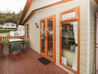 A wooden deck with table and chairs outside a house with wooden framed windows and door at 16 Heritage Park Heritage Park near Kilgetty