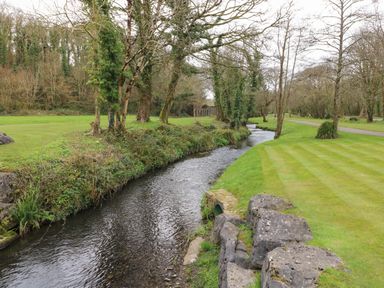 A narrow river flowing through a park with grass and trees at 16 Heritage Park Heritage Park near Kilgetty