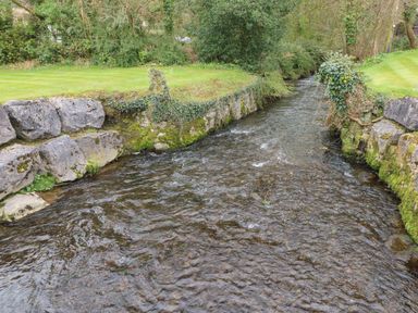 A narrow stream with stone walls on both sides and grass and trees in the background at 16 Heritage Park in Heritage Park near Kilgetty