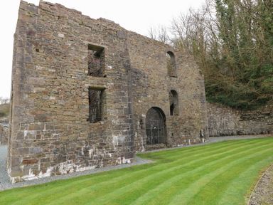An old stone ruin with arched openings and a gated entrance surrounded by grass and trees at 16 Heritage Park in Heritage Park near Kilgetty