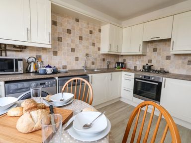 A kitchen with white cabinets a tiled backsplash an oven a washing machine a microwave and a table set with bowls glasses and bread at Amaranta Brewers Quay Harbour