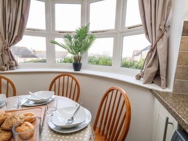 A dining area with a round table set with bowls spoons and glasses near a bay window with curtains and a potted plant at Amaranta Brewers Quay Harbour