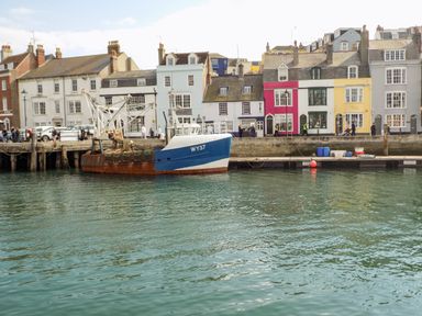 A fishing boat docked at a waterfront with colorful houses and people walking at Brewers Quay Harbour