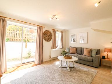 A living room with a gray sofa pillows a white round coffee table rug and sliding glass doors at Amaranta Brewers Quay Harbour