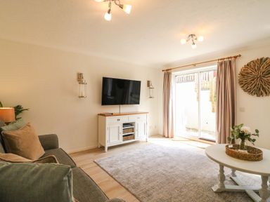 A living room with a sofa a wall mounted tv a white tv unit and a round coffee table with flowers at Amaranta in Brewers Quay Harbour