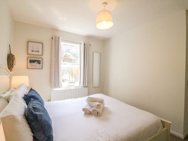 A bedroom with a bed with white linens and blue pillows a window with striped curtains and framed pictures at Amaranta in Brewers Quay Harbour