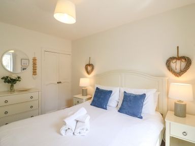 A bedroom with a bed with blue pillows lamps on bedside tables and a dresser with a round mirror at Amaranta Brewers Quay Harbour