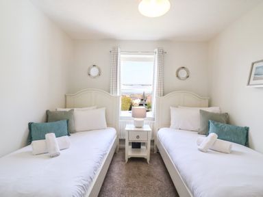 A bedroom with two single beds pillows and rolled towels a central bedside table and a window with curtains at Amaranta Brewers Quay Harbour