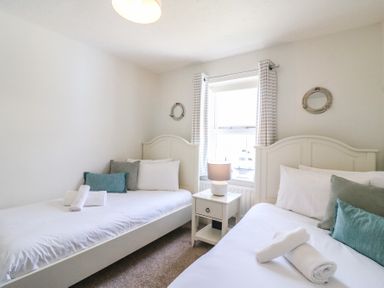 A bedroom with two single beds a bedside table with lamp and a window with striped curtains at Amaranta Brewers Quay Harbour