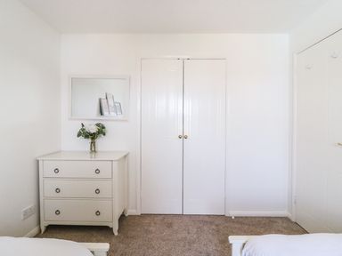 A bedroom corner with a white chest of drawers a vase with flowers a mirror and closed white double closet doors at Amaranta in Brewers Quay Harbour