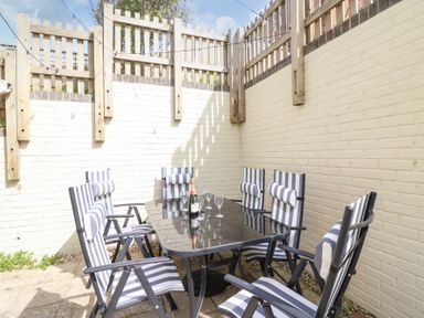 An outdoor patio with a black glass table and six striped chairs against pale brick walls at Amaranta Brewers Quay Harbour