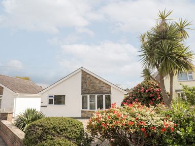 A white house with a triangular roof and a garden with bushes and flowering plants at 31 Beach Road Morfa Bychan