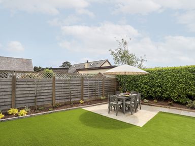 A garden with a patio table and chairs under an umbrella surrounded by a wooden fence and hedge at 31 Beach Road Morfa Bychan