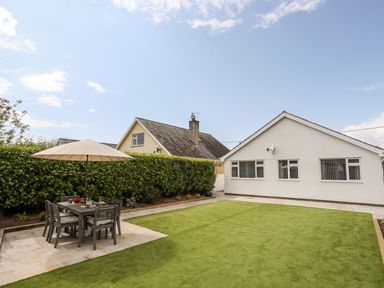 A backyard with a dining table and umbrella on a tiled area and a white house in the background at 31 Beach Road Morfa Bychan
