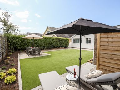A backyard with lounge chairs under an umbrella and a dining table with an umbrella at 31 Beach Road in Morfa Bychan