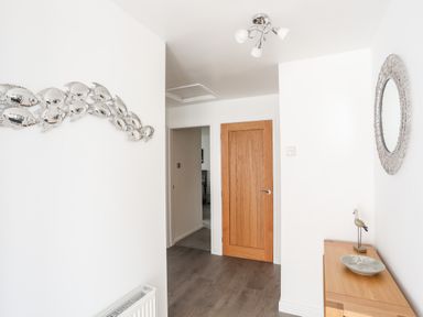 A hallway with a wooden door wooden console table with a decorative bird and plate round mirror and metallic fish wall art at 31 Beach Road in Morfa Bychan