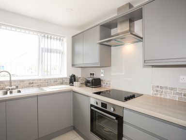 A kitchen with grey cabinets a stovetop oven kettle toaster and sink at 31 Beach Road Morfa Bychan