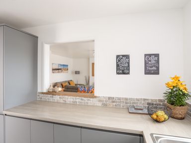 A kitchen counter with a fruit basket a plant and two coffee signs on the wall at 31 Beach Road in Morfa Bychan