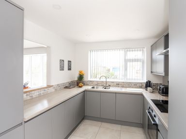 A modern kitchen with grey cabinets a sink oven kettle and toaster at 31 Beach Road in Morfa Bychan