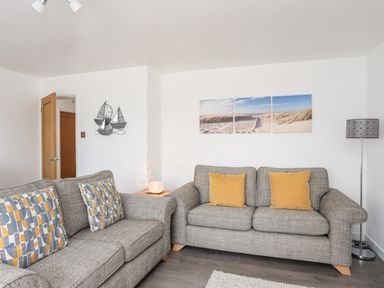 A living room with two grey sofas and patterned cushions and a beach picture on the wall at 31 Beach Road in Morfa Bychan