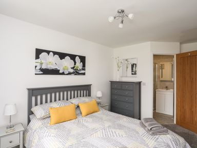 A bedroom with a bed with yellow pillows and gray bedding a gray dresser a nightstand with a lamp and an open door leading to a bathroom at 31 Beach Road in Morfa Bychan