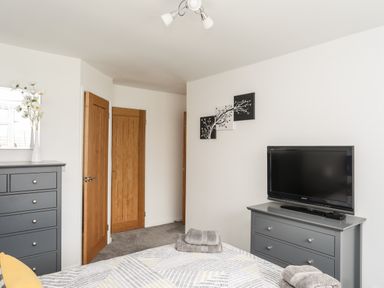 A bedroom with a bed folded towels on it a grey dresser with a television and a grey chest of drawers with a vase of flowers 31 Beach Road Morfa Bychan