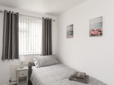 A bedroom with a single bed gray bedding a nightstand with lamp gray curtains and two pictures on the wall at 31 Beach Road in Morfa Bychan