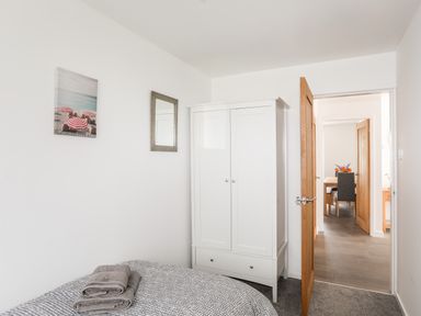 A bedroom with a bed, white wardrobe, gray towels, and a doorway showing a dining area at 31 Beach Road in Morfa Bychan