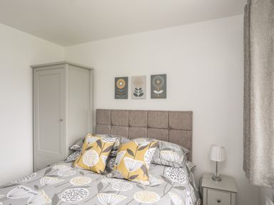 A bedroom with a bed featuring yellow and gray floral bedding a gray wardrobe and a bedside table with a lamp at 31 Beach Road in Morfa Bychan