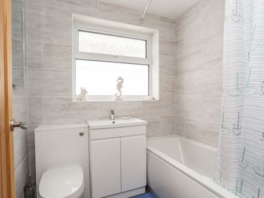A bathroom with a toilet sink cabinet bathtub and window at 31 Beach Road Morfa Bychan