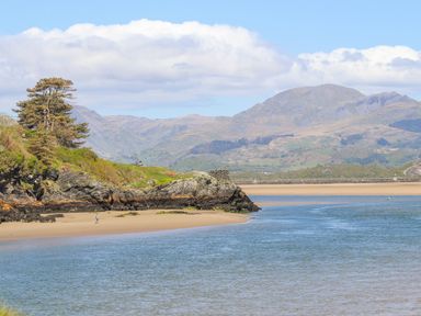 A river flowing past a sandy beach with rocky cliffs and hills in the background at 31 Beach Road in Morfa Bychan