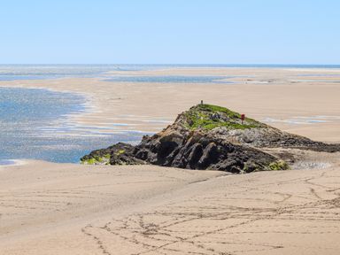 A sandy beach with a rocky outcrop covered in grass and the sea in the background at 31 Beach Road in Morfa Bychan