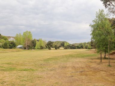 A grassy open field with scattered trees and a small building in the distance at 31 Beach Road in Morfa Bychan