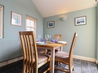 A dining area with a round wooden table and four chairs on a tiled floor at Faraway Cottage in St Levan near Porthgwarra