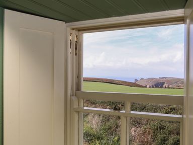 A view through an open window showing green fields and rocky hills at Faraway Cottage in St Levan near Porthgwarra