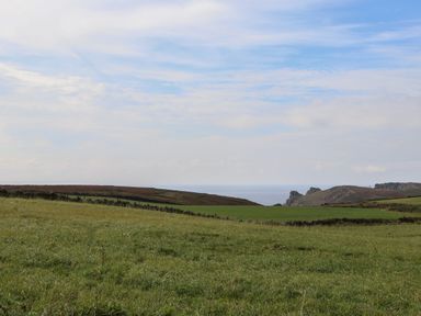 A grassy field with a stone wall and hills with rocky cliffs in the distance at Faraway Cottage in St Levan near Porthgwarra
